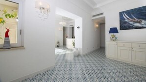 Un pasillo con baldosas de diseño, una pared blanca con un cuadro y un aparador con una lámpara azul.