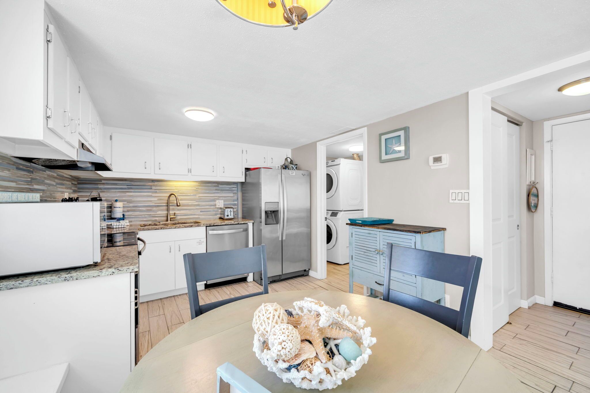 Une cuisine moderne avec des meubles blancs, des appareils en acier inoxydable et un coin repas comprenant une table et des chaises.