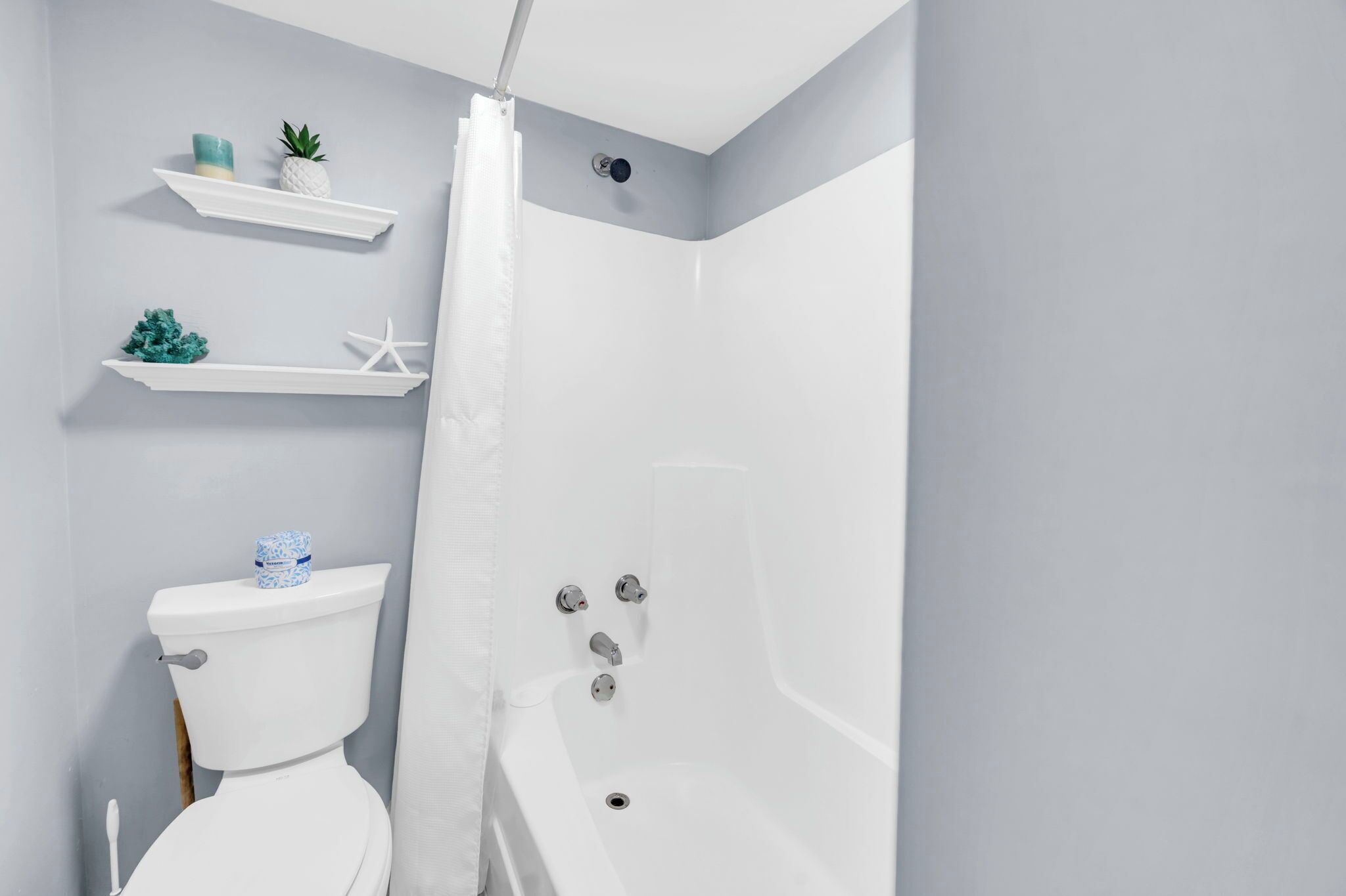 A bathroom with a toilet, a bathtub, and two shelves with decorative items.