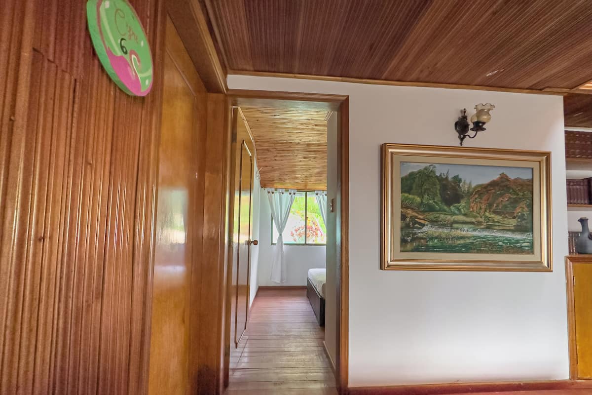 A wooden hallway with a painting on the wall, a door with a number sign, and a window with curtains.