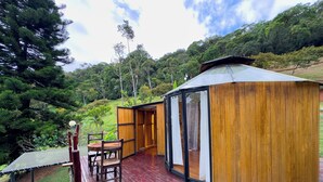 A wooden gazebo with a glass door, a wooden deck, and a table with chairs.