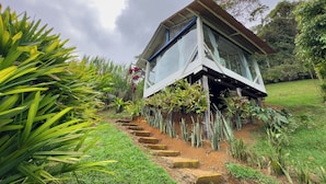 A small, elevated structure with a sloped roof, surrounded by lush greenery and a garden path leading to it.