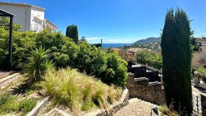 Una zona residencial en una ladera con vista al mar, muros de contención de piedra y un edificio blanco con balcones.