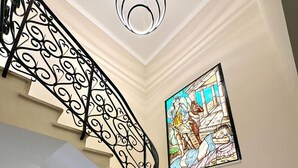 Una escalera con barandillas de metal negro ornamentado y un vitral que representa una escena clásica.