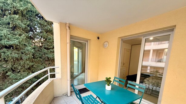 Un balcone con un tavolo e sedie color turchese, una pianta in vaso e vista su un albero e un edificio.