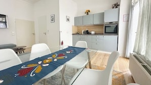 Una cucina moderna con mobili grigi, un forno a microonde e un piano cottura. Si nota un tavolo da pranzo con tovaglia blu e sedie bianche.