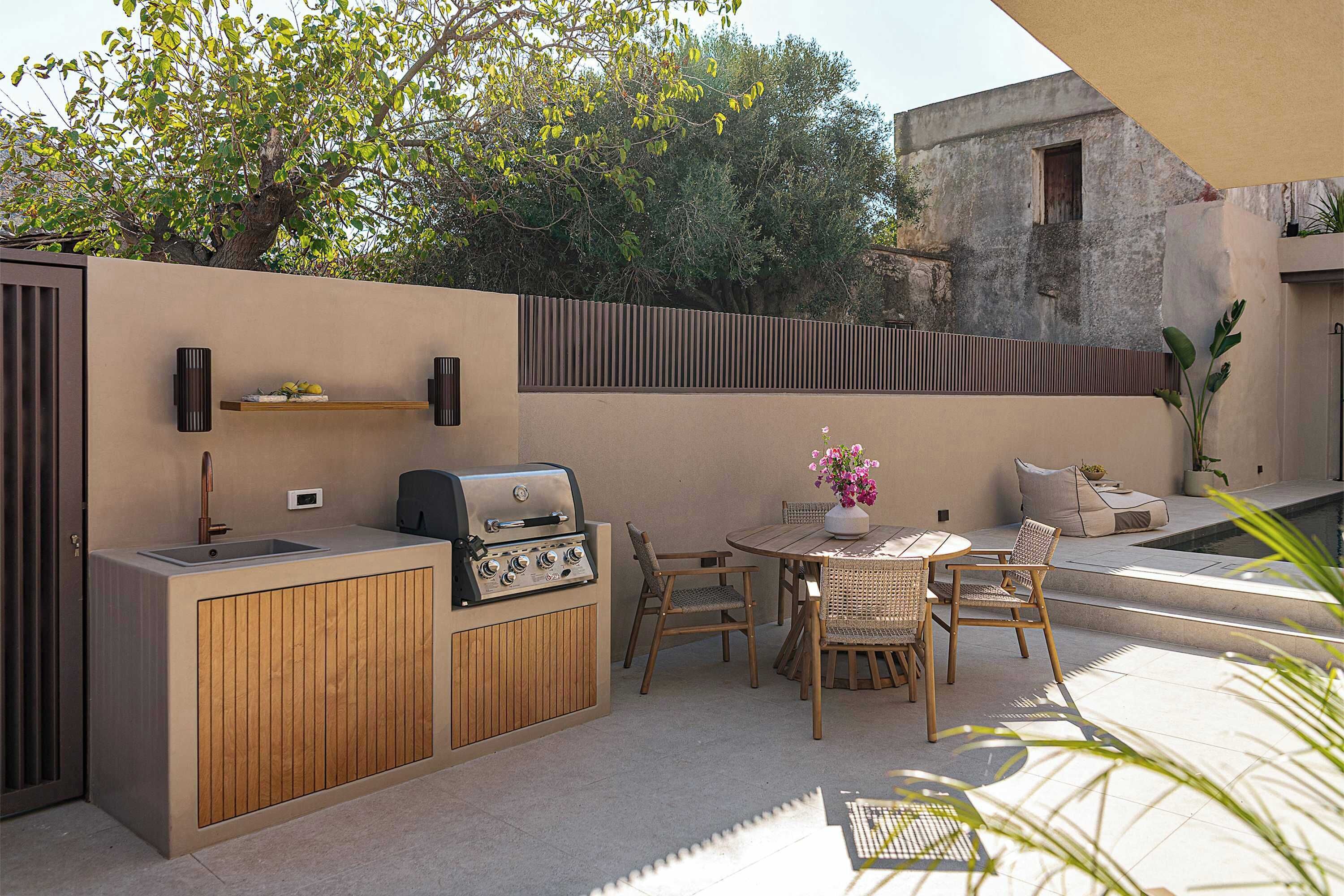 Una terrassa exterior amb una barbacoa integrada, zona de seients i una piscina petita.