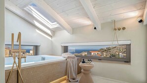 A modern bathroom with a skylight, a bathtub, and a view of a coastal town. - Villa Villagio Rosso (Kokkino Chorio)