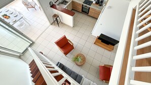 Una cocina moderna con una isla central, un comedor con una mesa dispuesta para cuatro personas y una escalera que sube a un nivel superior.