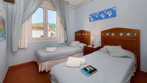 Une chambre avec deux lits, une fenêtre avec des rideaux, une tête de lit en bois, une table de chevet avec une lampe et une œuvre d’art murale.