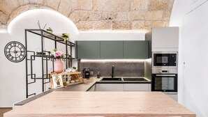 Una cocina moderna con una isla de madera, dos sillas rosas, un reloj y una pared de ladrillo.