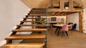 Un interior moderno con una escalera de madera, un área de comedor con sillas rosadas y una cocina con armarios de madera.