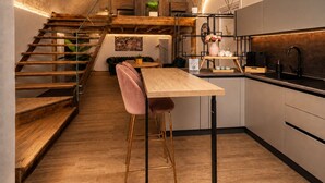 Una cocina moderna con una mesa de madera, taburetes de bar, una escalera y una isla de cocina con un lavabo y una cafetera.