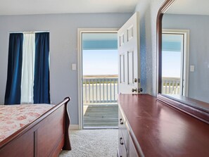 A bedroom with a bed, dresser, and a door leading to a balcony with a view of the beach. - Your Dream Colorado River Getaway! Great Fishing - Family fun! Minutes to Beach! (Matagorda)