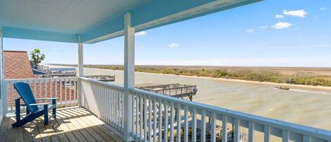 A wooden deck with a railing, a blue chair, and a view of a river with a boat.