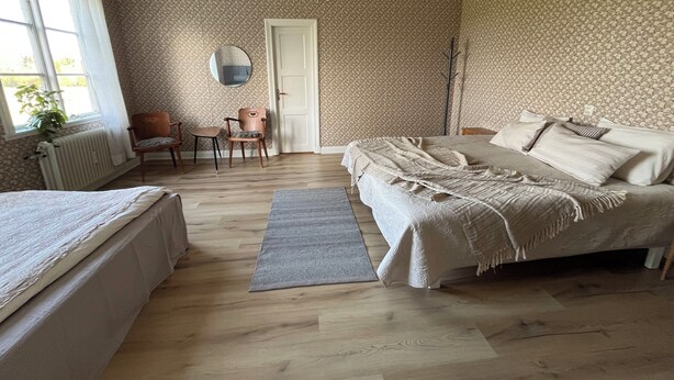 A bedroom with two beds, a sitting area with chairs, a radiator, a mirror, and patterned wallpaper. - Apartment at country side. Spa facility and much more out in swedish woods. (säffle)