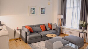 A modern living room with a grey sofa, a round coffee table, and a glass-top dining table. - Family Apartment in Berlin for 6 – Central & Quiet, Supermarket & Park Nearby (Berlin)