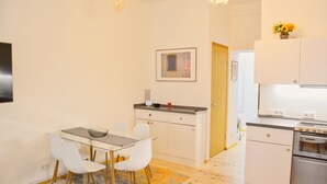 A modern kitchen with white cabinets, a built-in oven, and a dining area with a glass table and white chairs. - Family Apartment in Berlin for 6 – Central & Quiet, Supermarket & Park Nearby (Berlin)