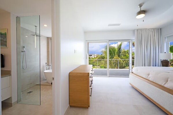 A modern bathroom with a glass shower enclosure, a wooden vanity, and a large window offering a view of palm trees and a clear sky.
