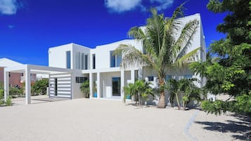 A modern white building with a covered outdoor area and palm trees.