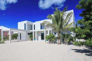 Un bâtiment moderne de couleur blanche, doté d’un espace extérieur couvert et agrémenté de palmiers.