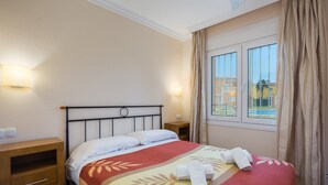 Quarto de hotel com cama, mesa de cabeceira, cômoda de madeira e janela com cortinas.