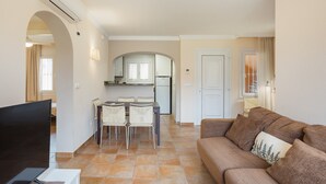 Uma sala de estar com sofá, TV e área de jantar com cadeiras e mesa.