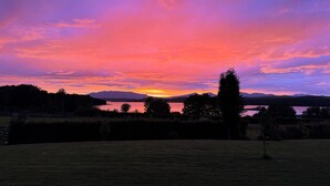 Ein Sonnenuntergang über einem See mit Bergen im Hintergrund und einem grasbewachsen Feld im Vordergrund.