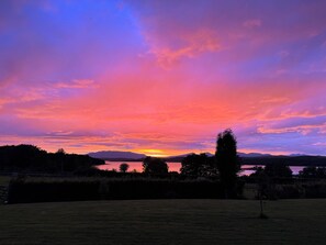 A sunset over a lake with mountains in the background and a grassy field in the foreground. - Còsagach 
Cosy one bedroom apartment. (Barcaldine)
