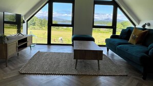 Ein modernes Wohnzimmer mit großem Fenster, einem Fernseher, einer Couch und einem Couchtisch.