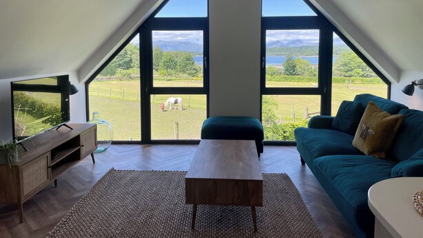 Ein geräumiges Schlafzimmer im Loft-Stil mit großen Dachfenstern, Holzboden, einem grünen Sofa und einem Fernseher auf einer Holzkommode.