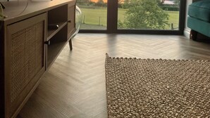 Ein Zimmer mit großem Fenster, das Blick auf einen Sonnenuntergang über einem See und Bergen bietet.