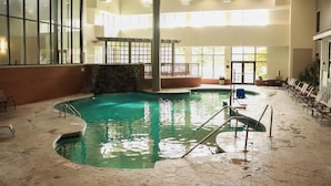 Une piscine intérieure à l’eau claire, entourée de carreaux de pierre et de rampes métalliques.
