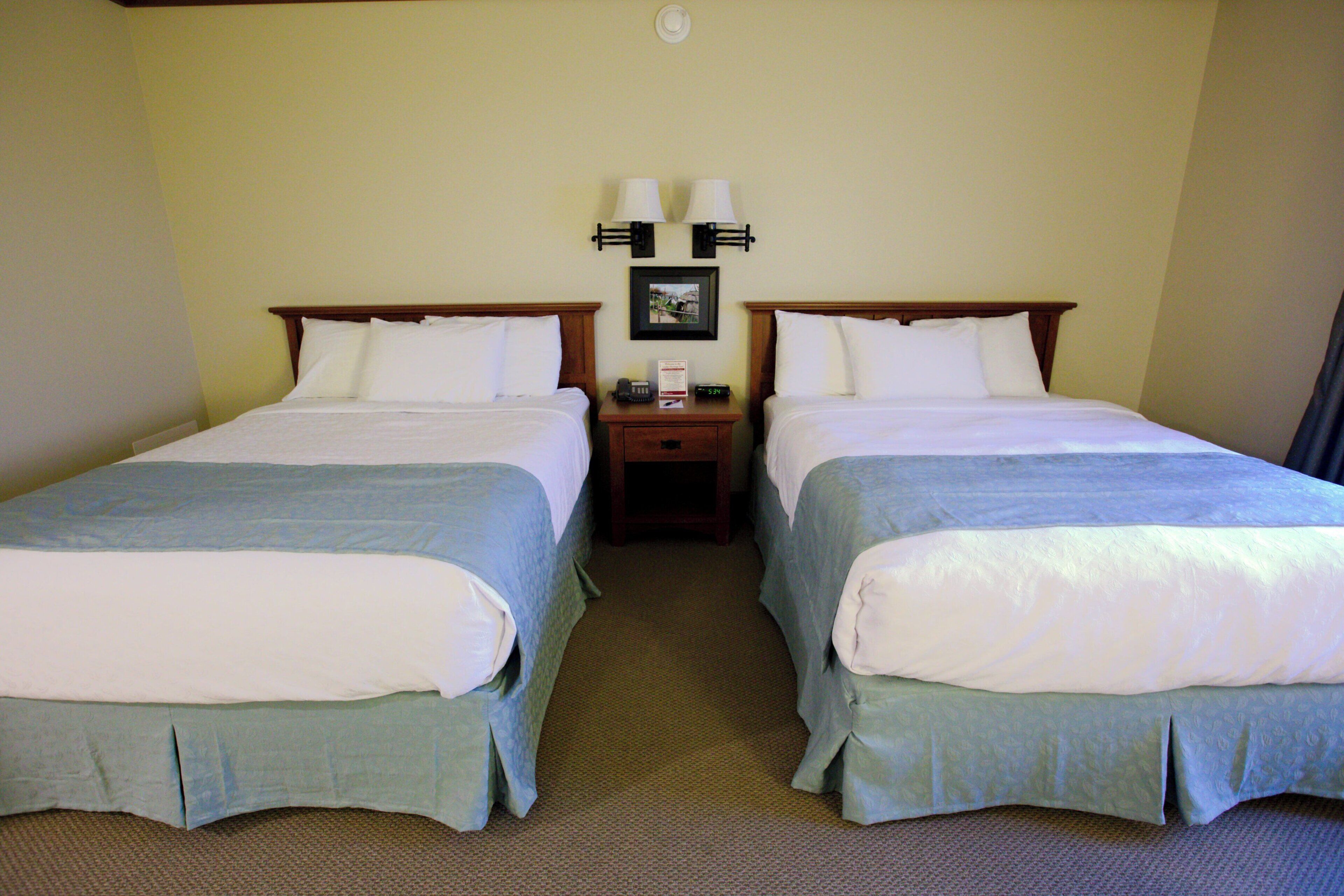 A hotel room with two beds, a nightstand with a lamp, and a framed picture on the wall.