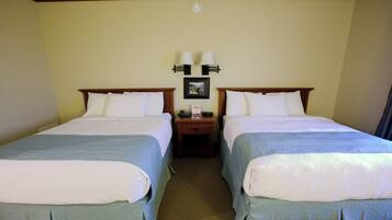 A hotel room with two beds, a nightstand with a lamp, and a framed picture on the wall.