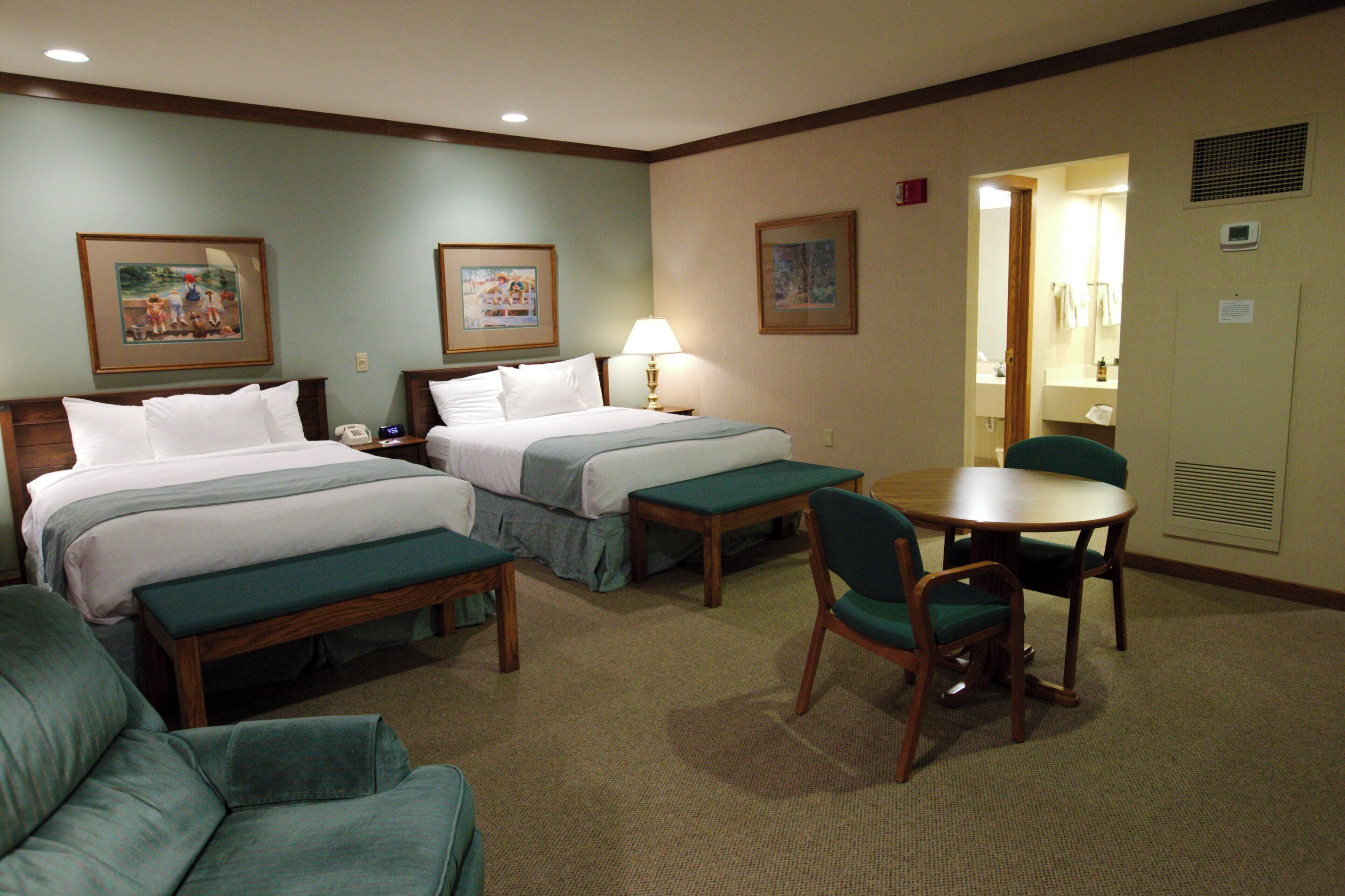A hotel room with two beds, a desk, a chair, and a small table.