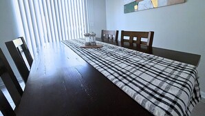 Ein Essbereich mit einem dunklen Holztisch, zwei Stühlen, einer gemusterten Tischdecke, einem Salz- und Pfefferset und einer Deckenleuchte.