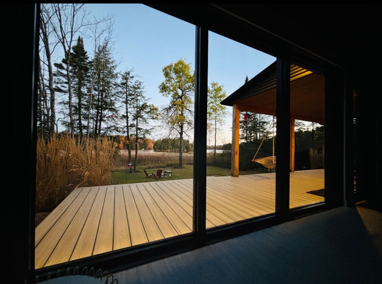 A modern house with a wooden deck, large windows, and a view of a forest.