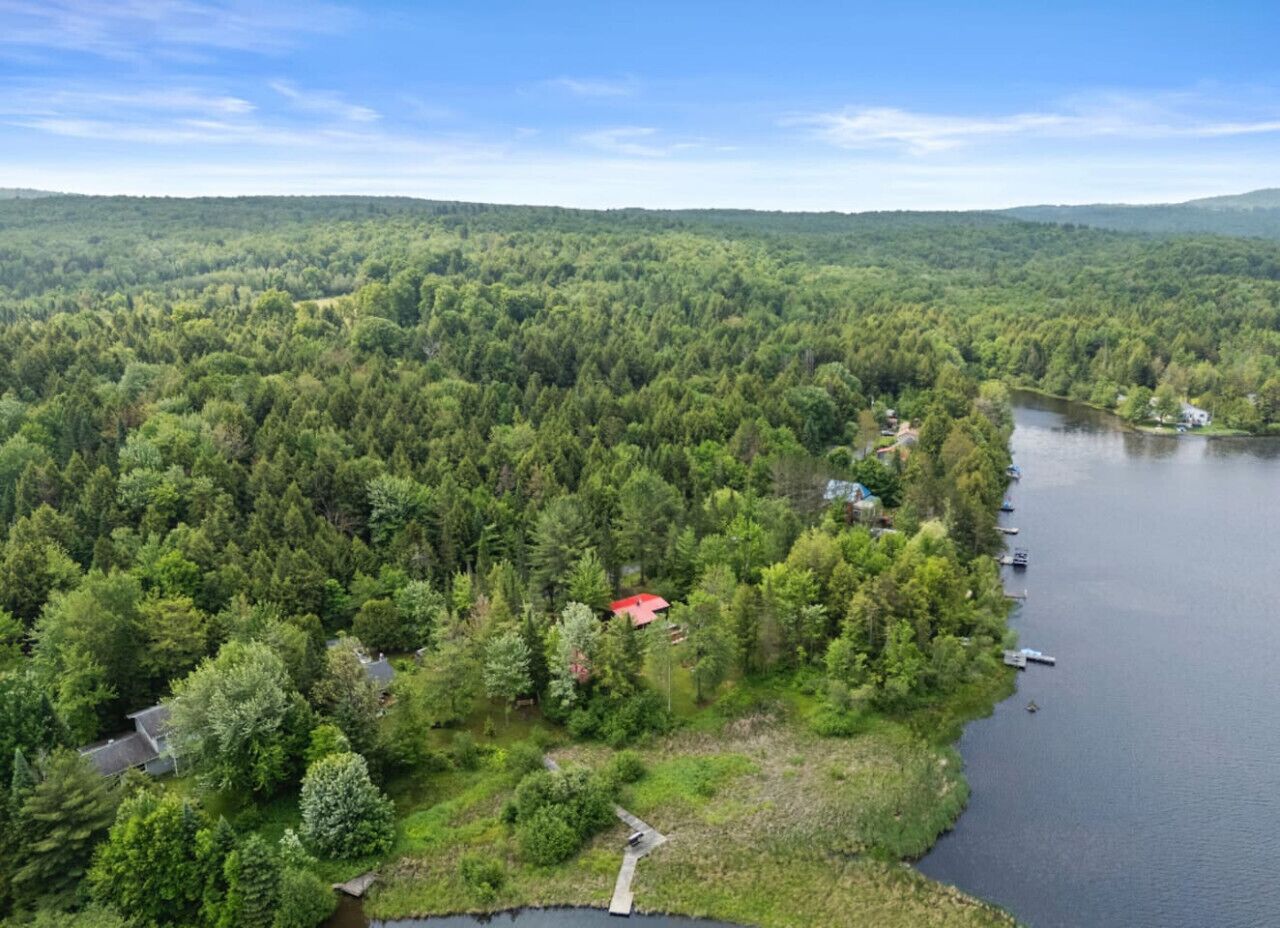 Ilmakuva metsäisestä alueesta, jossa on järvi, punakattoinen rakennus ja laituri, jossa on veneitä.