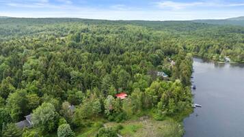 Ilmakuva metsäisestä alueesta, jossa on järvi, punakattoinen rakennus ja laituri, jossa on veneitä.