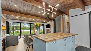 A modern kitchen with a wooden island, large windows, and a dining area with a view of greenery.