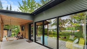 A modern house with a wooden deck, large sliding glass doors, and a hanging chair.