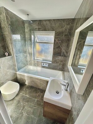 Ein modernes Badezimmer mit einer gläsernen Duschkabine, einer freistehenden Badewanne, einem Waschtisch und einer Toilette.