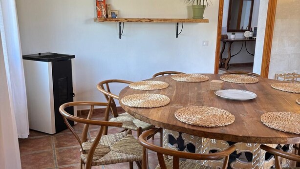 A dining area with a round wooden table, woven placemats, and wicker chairs.