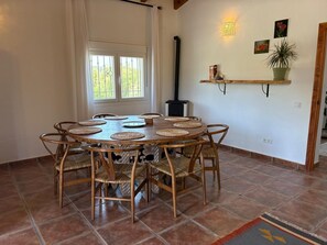 Een eetruimte met een ronde houten tafel, geweven placemats en rieten stoelen.