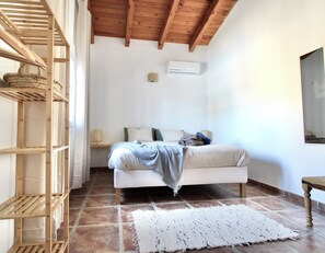 Een slaapkamer met een bed, een houten plank, een witte airconditioning en een betegelde vloer.
