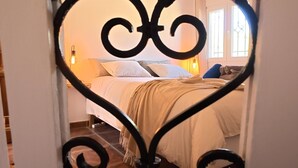 Una puerta con un marco metálico decorativo y vista a un dormitorio con cama, almohadas y mesita de noche.