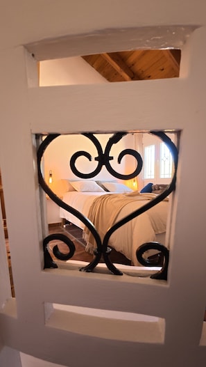 A door with a decorative metal frame and a view of a bedroom with a bed, pillows, and a nightstand.