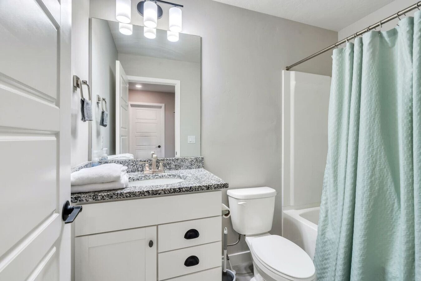 Une salle de bain avec un meuble-lavabo blanc, un évier, des toilettes et un rideau de douche.