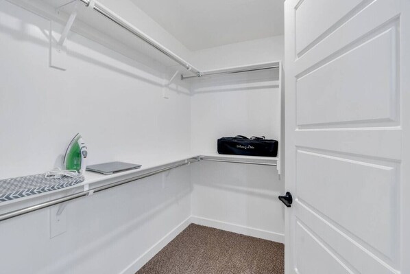 A white closet with a hanging rack, a green iron, and a black bag.